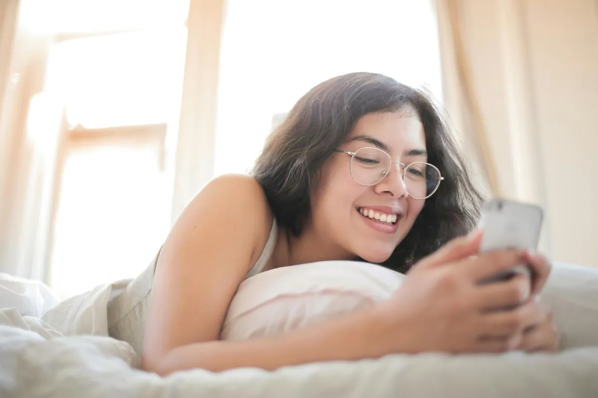 Person smiling while reading a message on their phone in bed
