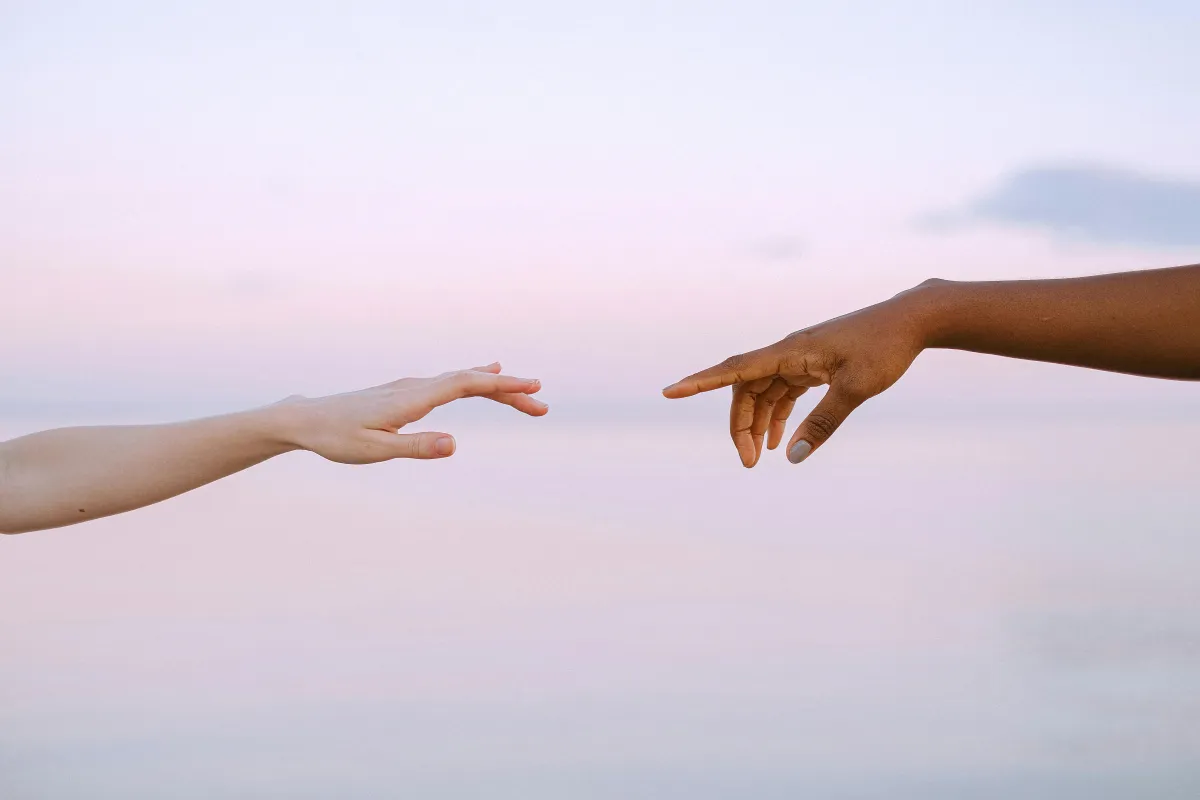Two hands reaching toward each other across a soft pink sky